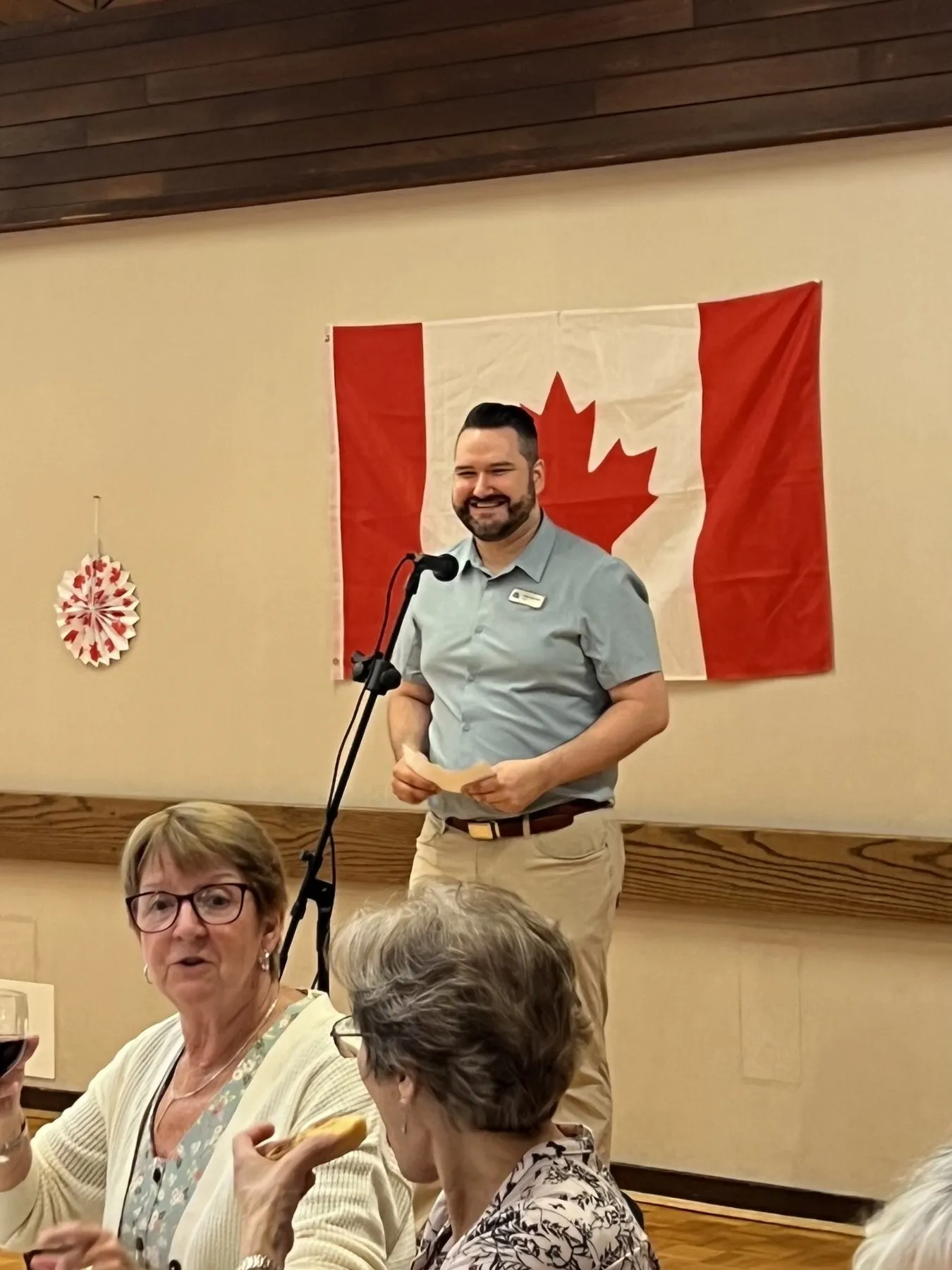 Callan Morrison speaking at a community event beside the Canadian flag.